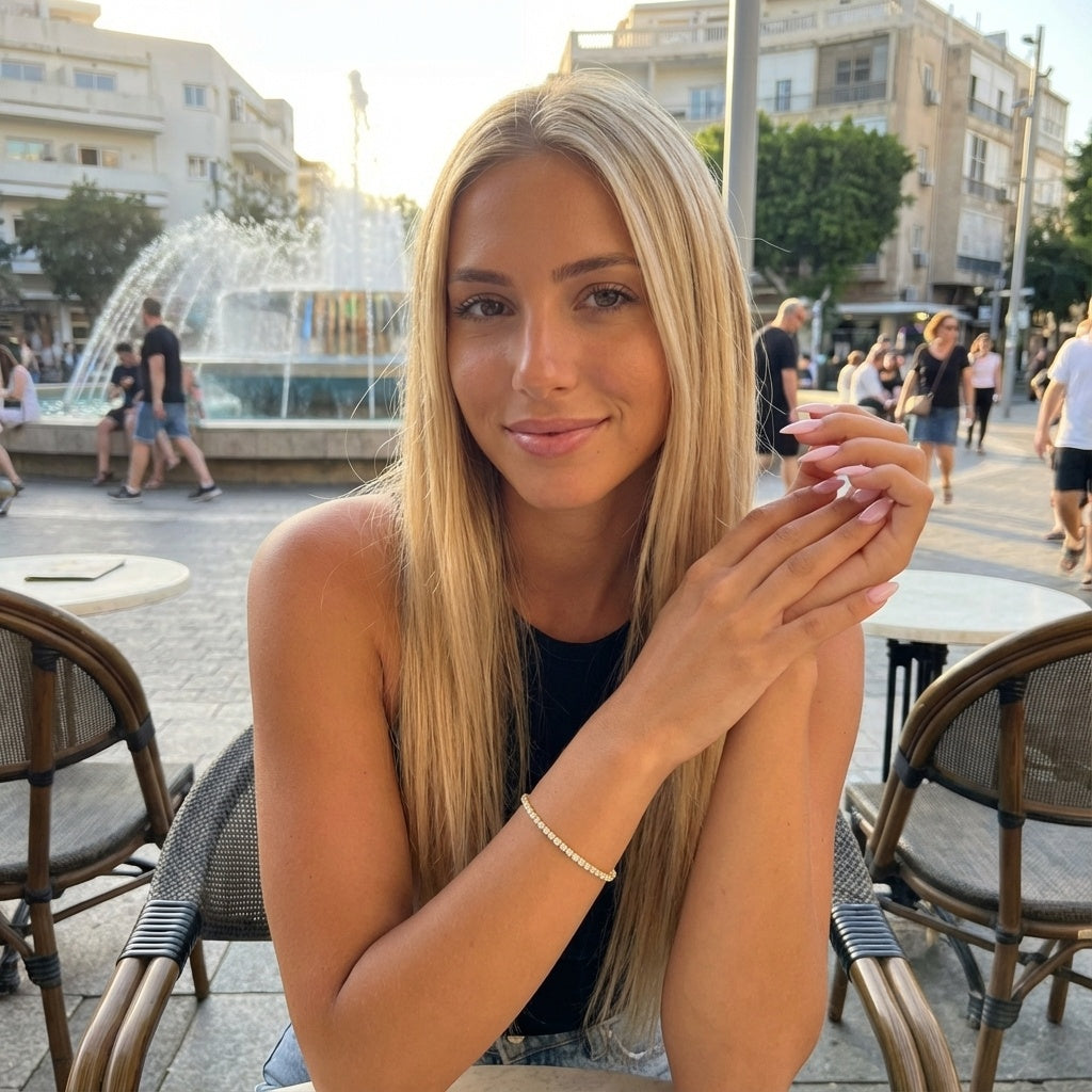 אישה בלונדינית בת 27 לובשת תקריב של צמיד טניס עשוי פליז בציפוי זהב 14 קראט עם שיבוץ אבני קריסטל איכותיות ואורך מתכוונן של 15 פלוס 5 סנטימטרים.