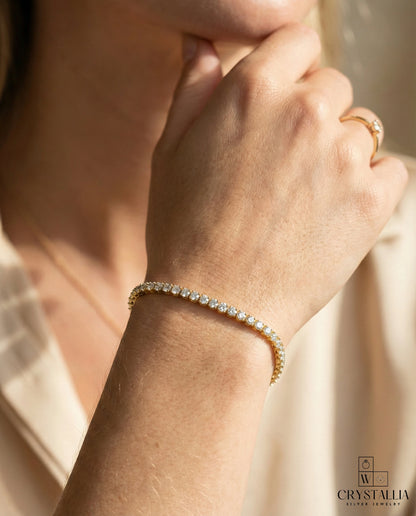 יש אישה עם צמיד טניס מעוצב בגימור כסוף עם שיבוץ רציף של אבנים נוצצות, דגם ZSI055-3-2mm מבית מותג התכשיטים קריסטליה על רקע נקי.