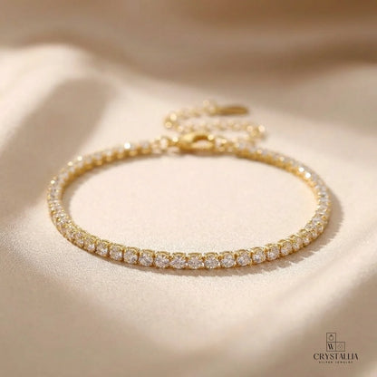 תקריב של צמיד טניס עשוי פליז בציפוי זהב 14 קראט עם שיבוץ אבני קריסטל איכותיות ואורך מתכוונן של 15 פלוס 5 סנטימטרים.