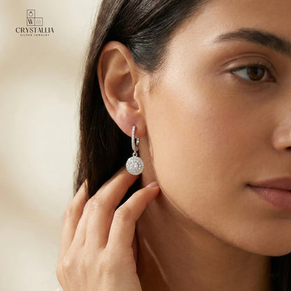 זוג עגילי כסף אמיתי 925 בסגנון נופל ומוארך, משובצים באבני זרקון מנצנצות לכל אורכם, צילום תקריב של תכשיטי קריסטליה.