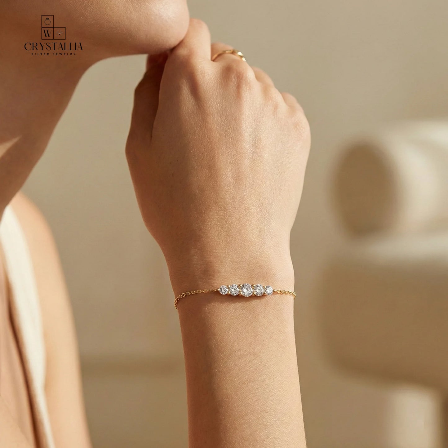 יש של אישה מודל עם צמיד מעוצב דגם  עשוי פליז בציפוי זהב 14K איכותי עם שיבוץ אבני קריסטל מנצנצות לאורך הצמיד על רקע נקי.